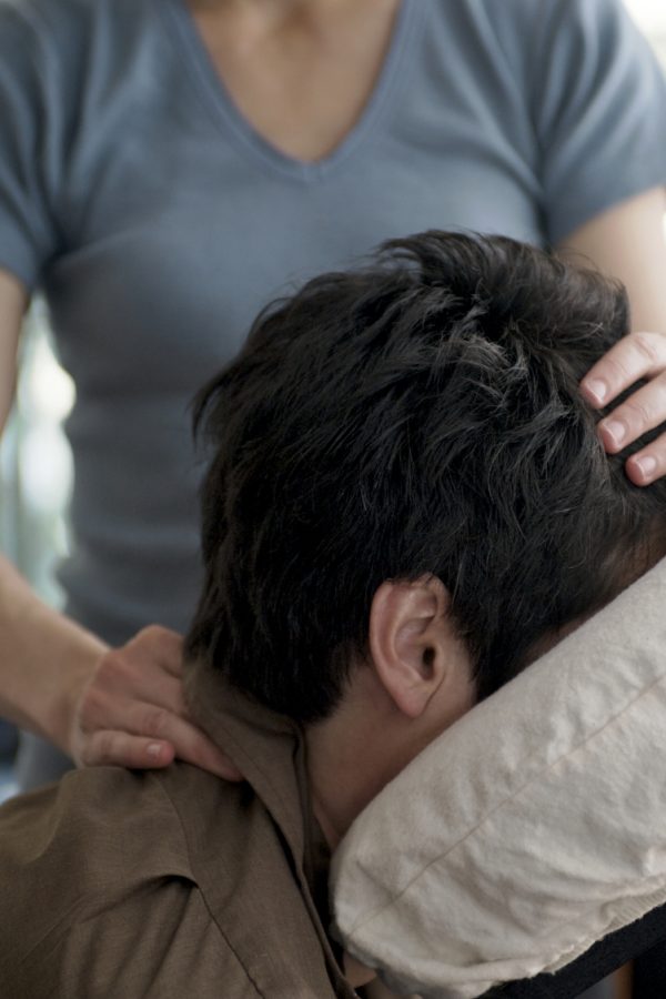 A man receives a chair massage from a mobile massage therapist in a pleasant office environment.
